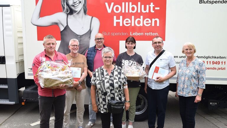 Ingrid Krause gratuliert sechs Blutspendern mit Geschenkkörben und Gutscheinen vor einem Blutspendefahrzeug