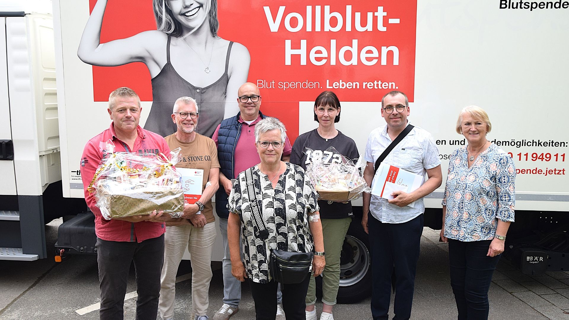Ingrid Krause gratuliert sechs Blutspendern mit Geschenkkörben und Gutscheinen vor einem Blutspendefahrzeug