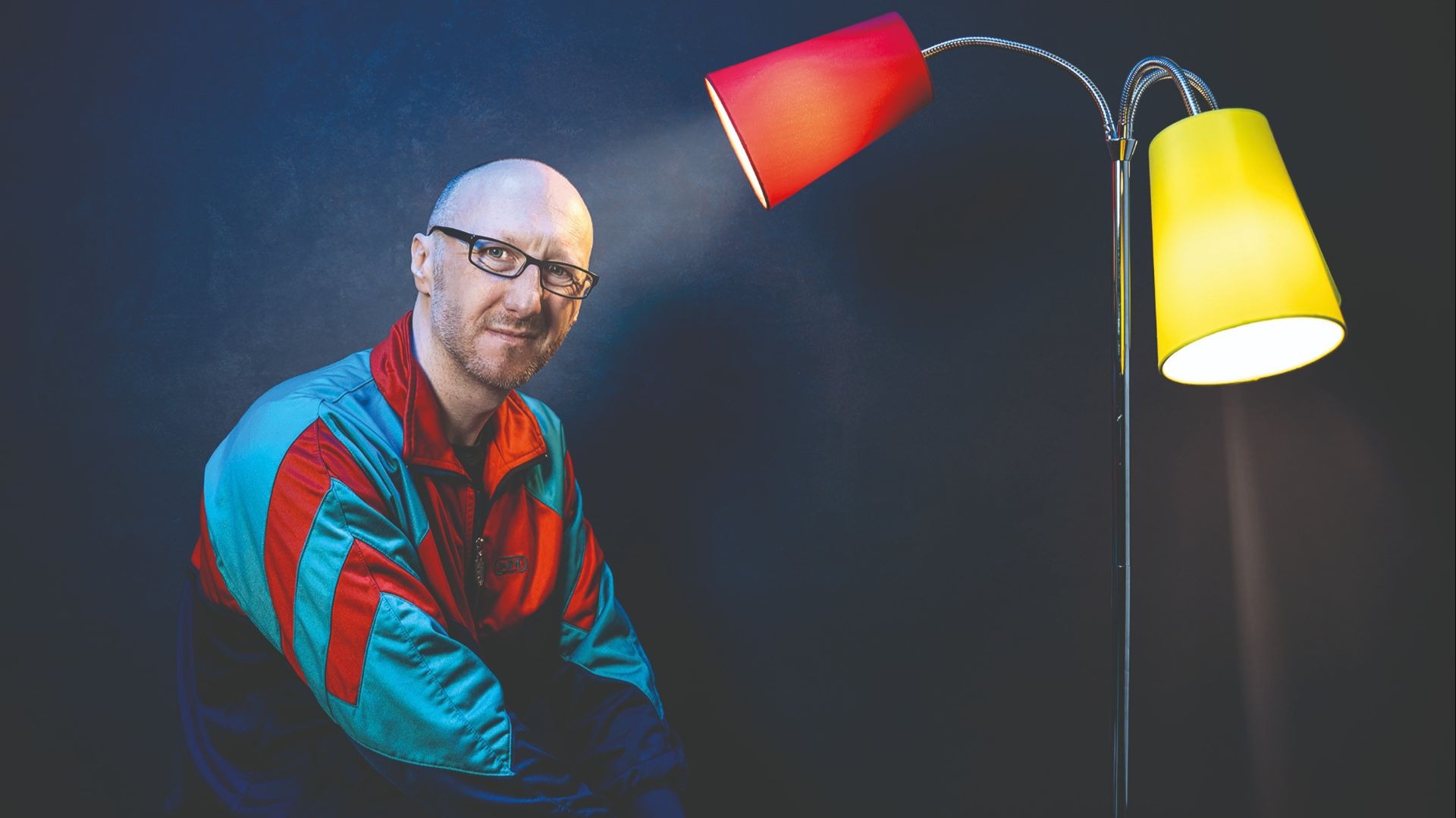 Ralf Senkel im bunten Trainingsanzug blickt in die Kamera, beleuchtet von einer roten und gelben Lampe
