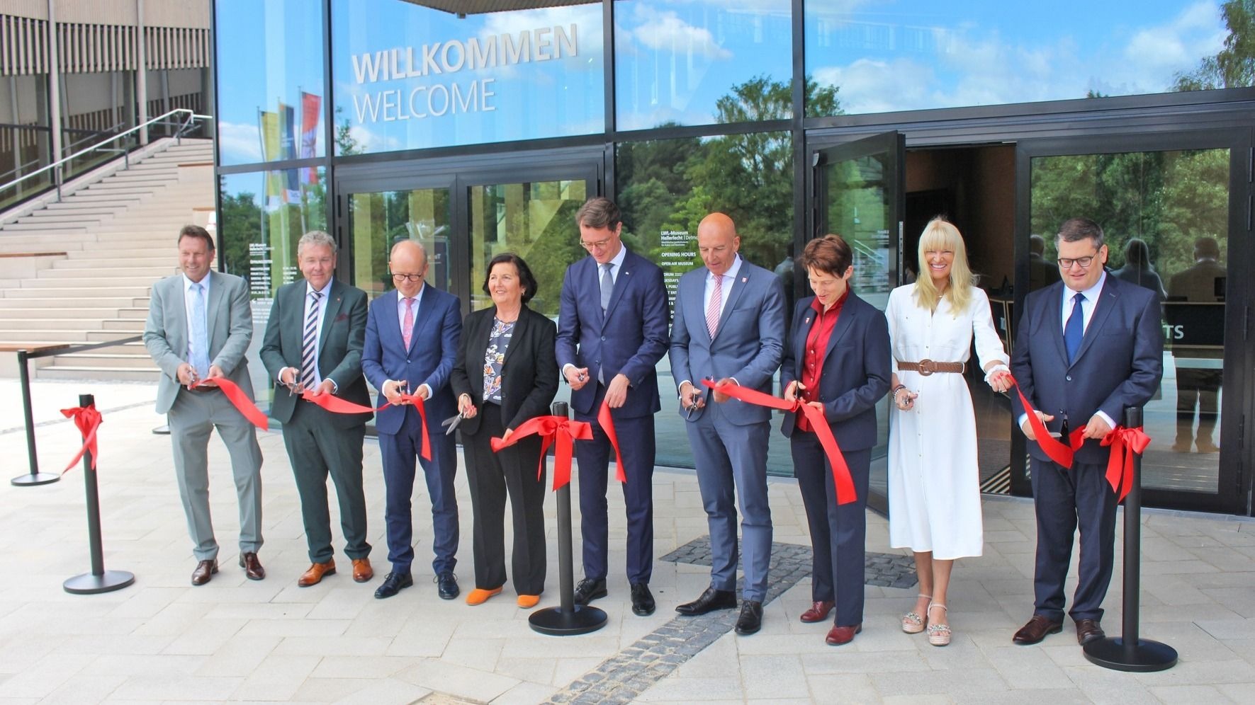 Neun Personen schneiden bei der feierlichen Eröffnung des neuen Eingangsgebäudes des LWL Museums Hellerlecht rote