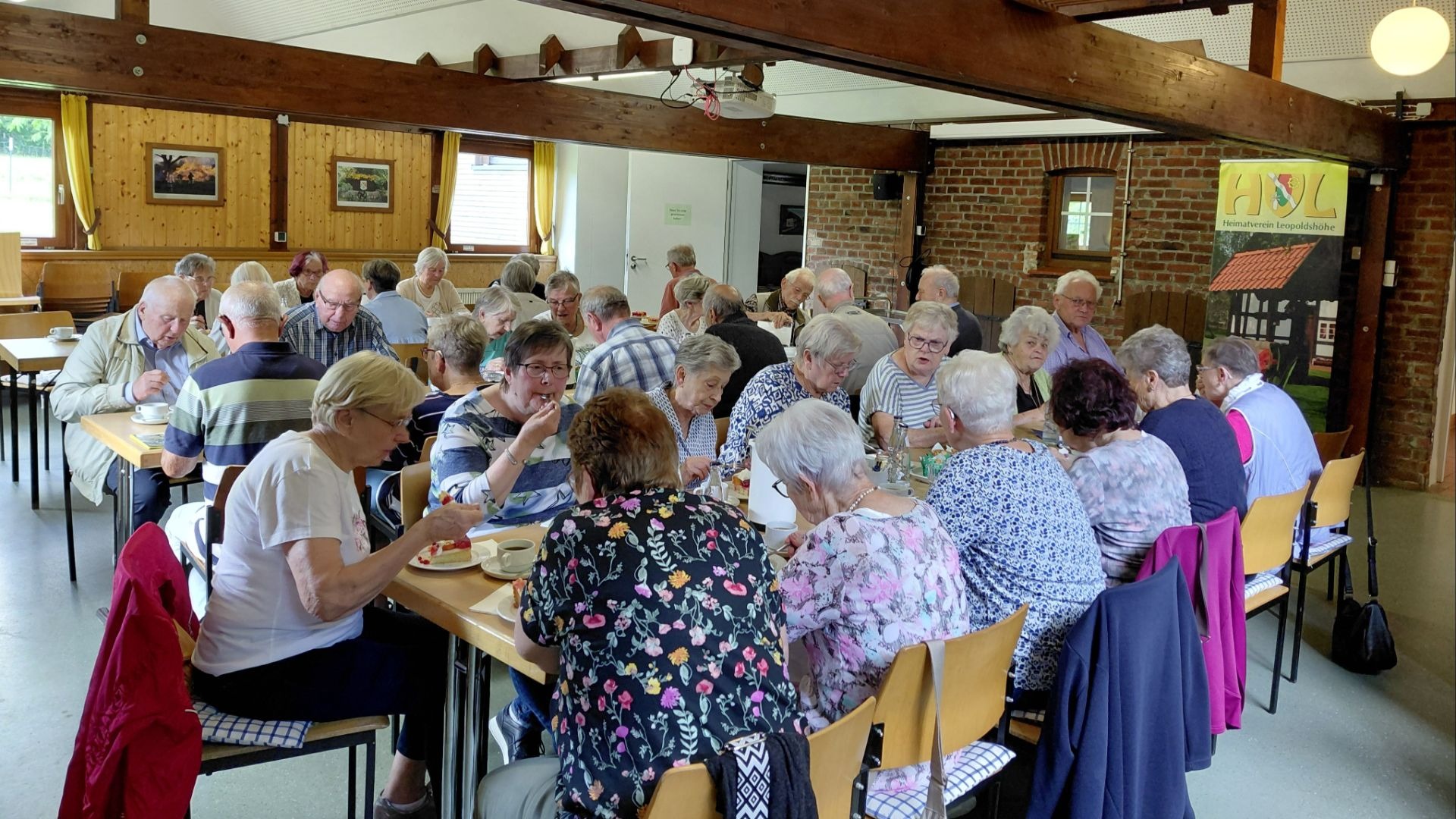 Senioren sitzen an Tischen im Backhaus, essen Kuchen und trinken Kaffee beim Klönnachmittag des Heimatvereins