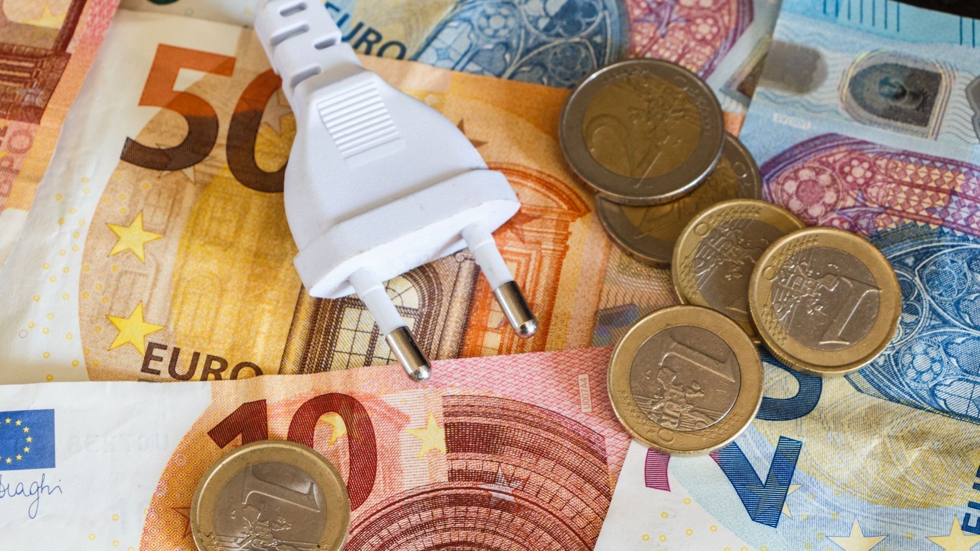 Weißer Stromstecker auf gemischten Euro-Scheinen und -Münzen