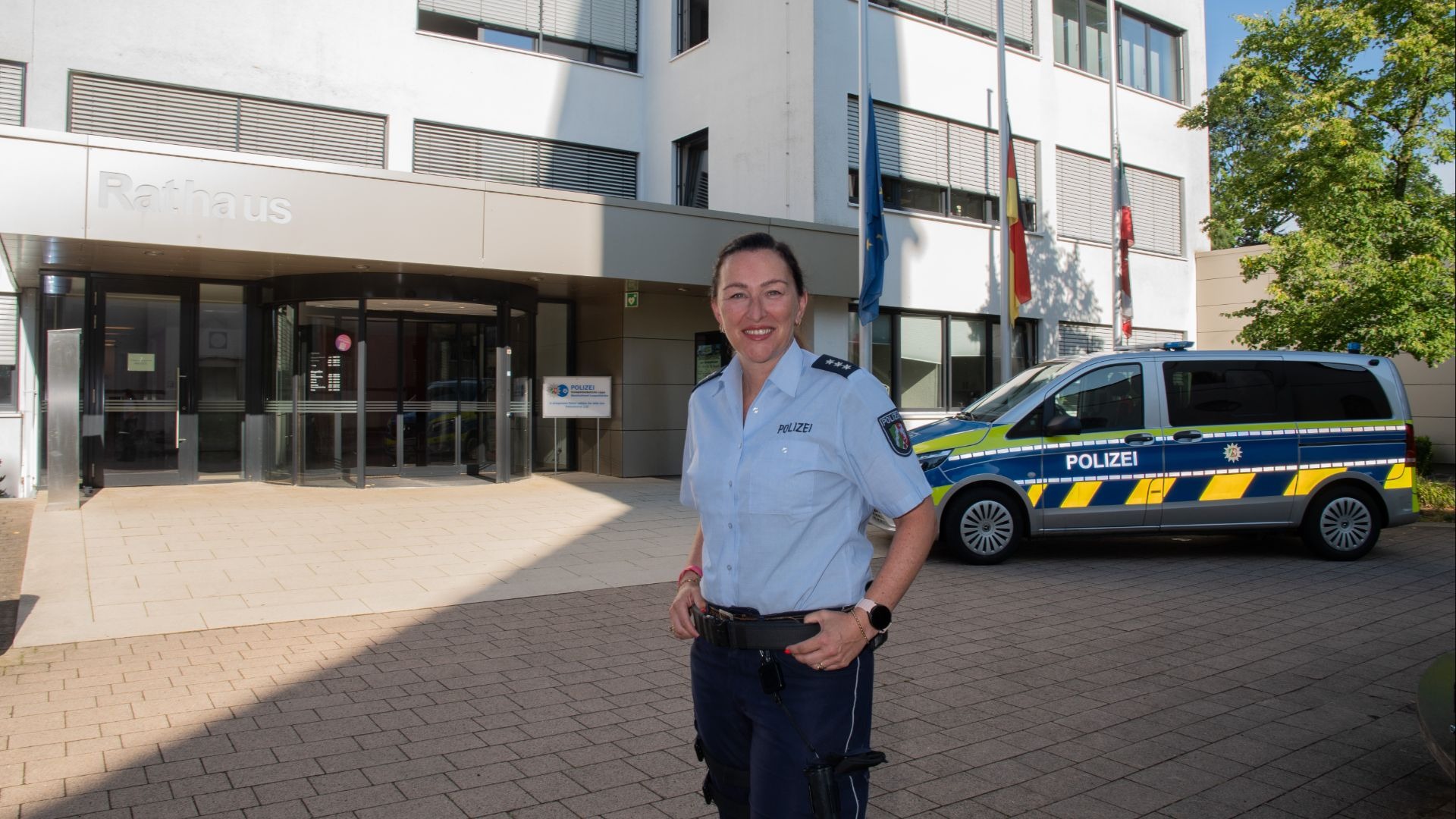 Roxana Keil-Preuß in Polizeiuniform lächelt vor dem Rathaus und einem Polizeiwagen
