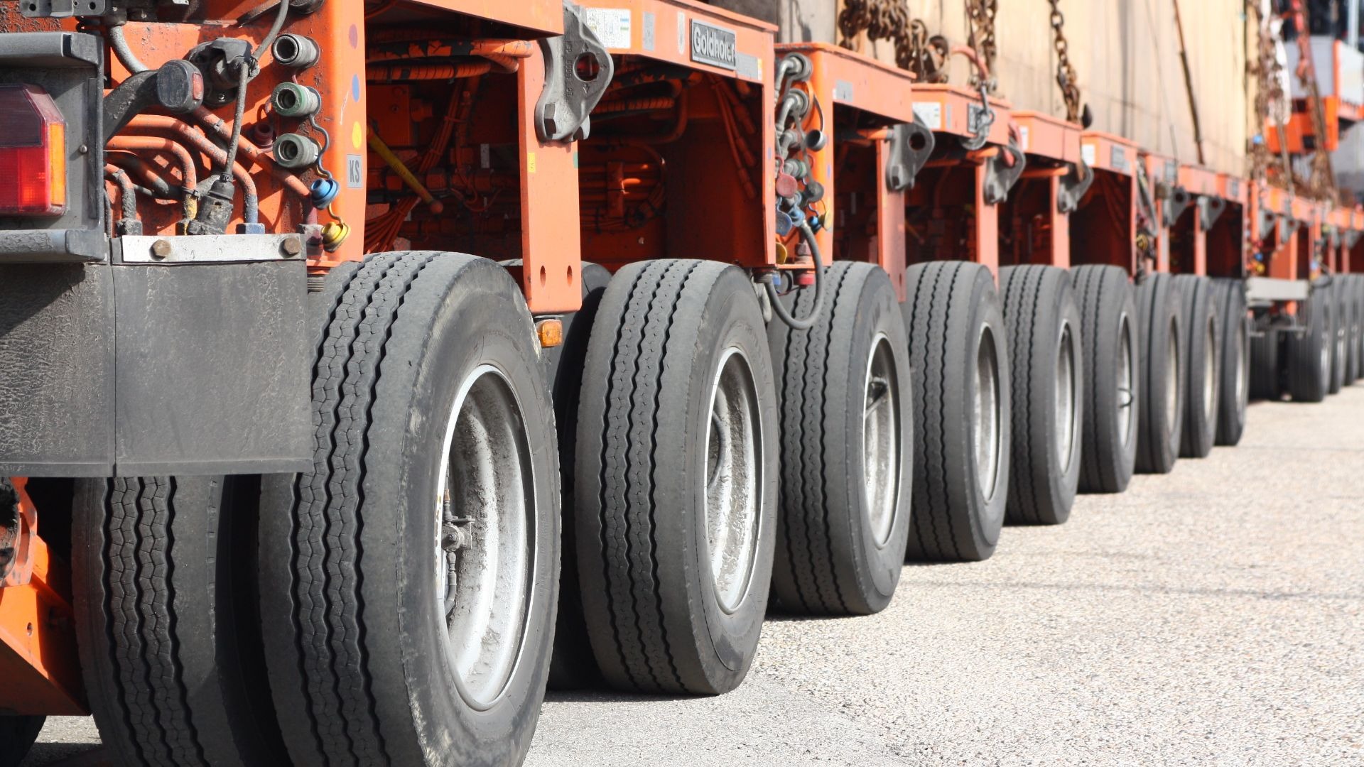 Reihen von schwarzen Reifen und orangefarbenen Achsen eines Schwerlasttransporters auf Asphalt