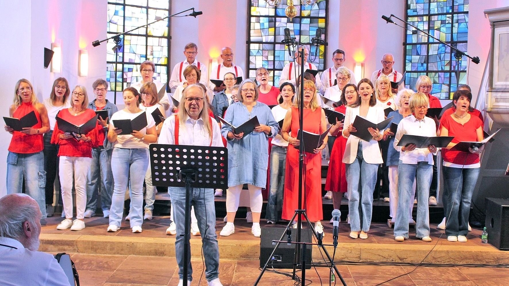 Der Leopoldshöher Projektchor singt mit Notenblättern in den Händen in einer Kirche mit Buntglasfenstern