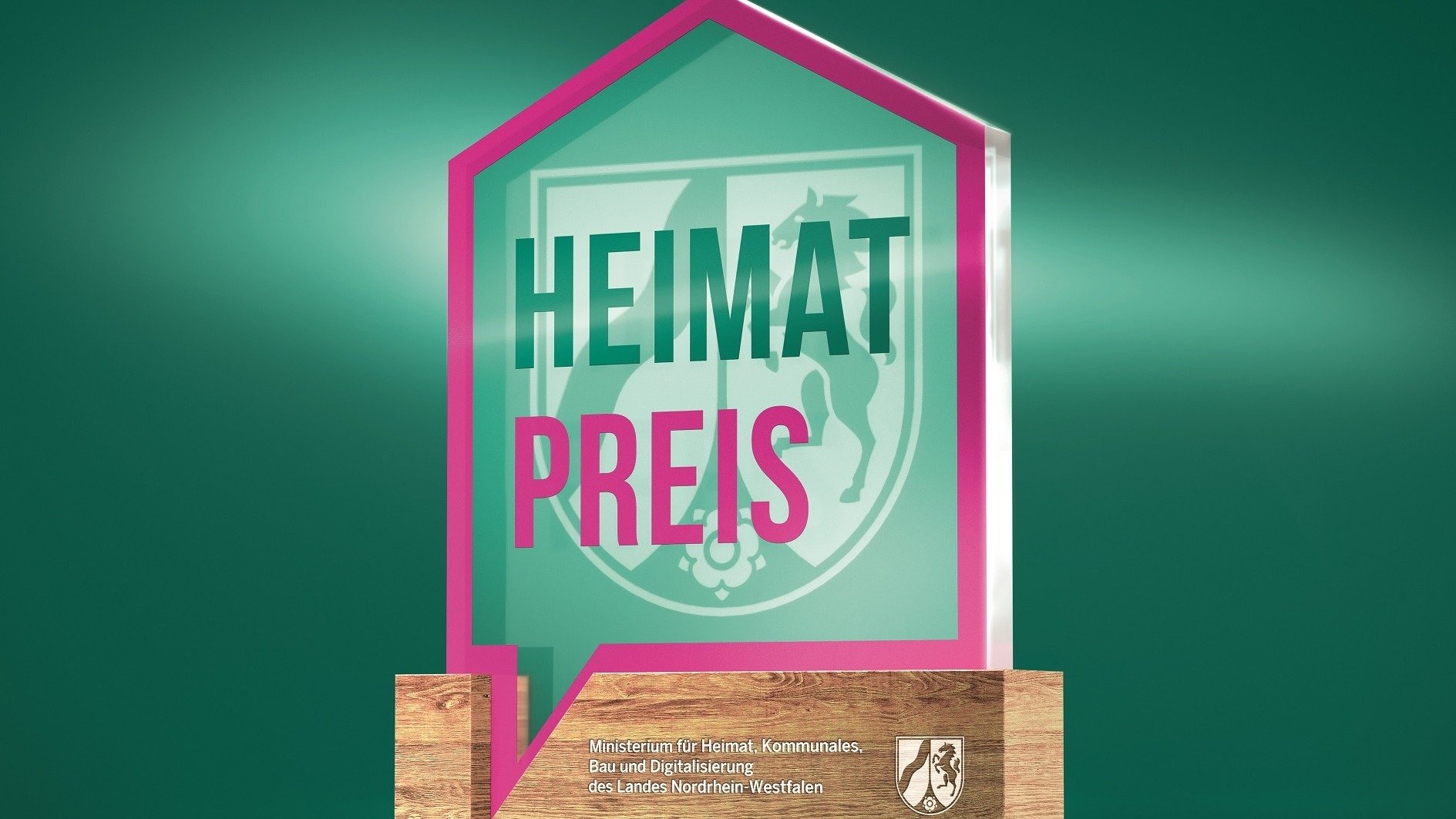 Hausförmiges 3D-Logo mit der Aufschrift HEIMAT PREIS und dem Wappen von Nordrhein-Westfalen auf einem Holzsockel