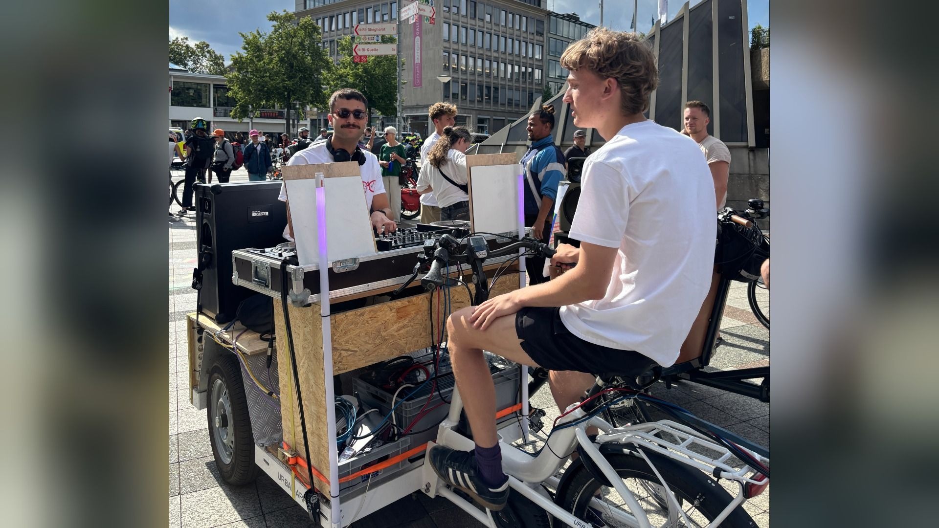 Ein Mann legt mit Kopfhörern und DJ-Pult Musik auf einem umgebauten Fahrrad mit Lautsprechern für eine Party auf der