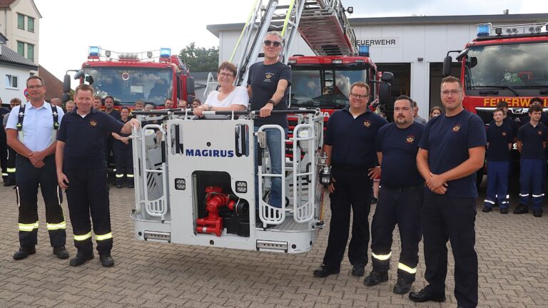 Jochen Tilleke und eine Frau im Korb einer Feuerwehrleiter, umringt von Feuerwehrleuten vor roten Löschfahrzeugen
