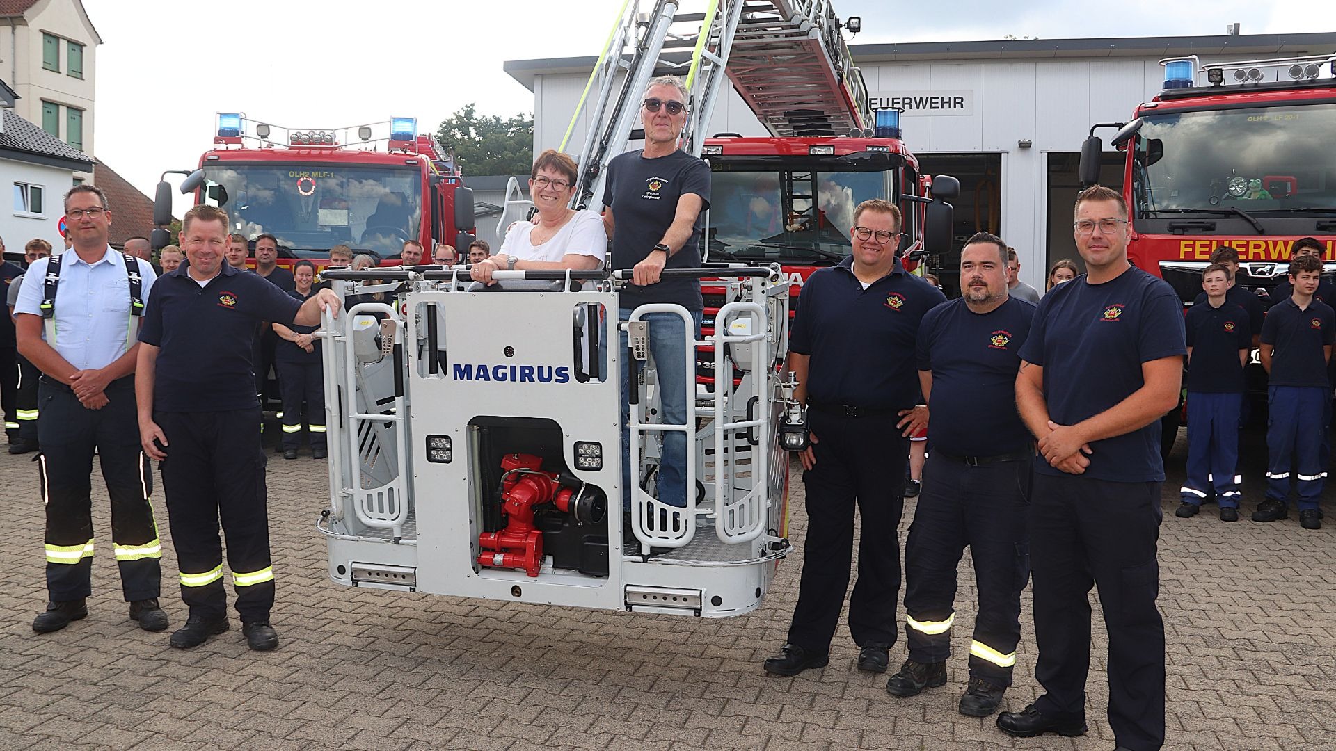 Jochen Tilleke und eine Frau im Korb einer Feuerwehrleiter, umringt von Feuerwehrleuten vor roten Löschfahrzeugen