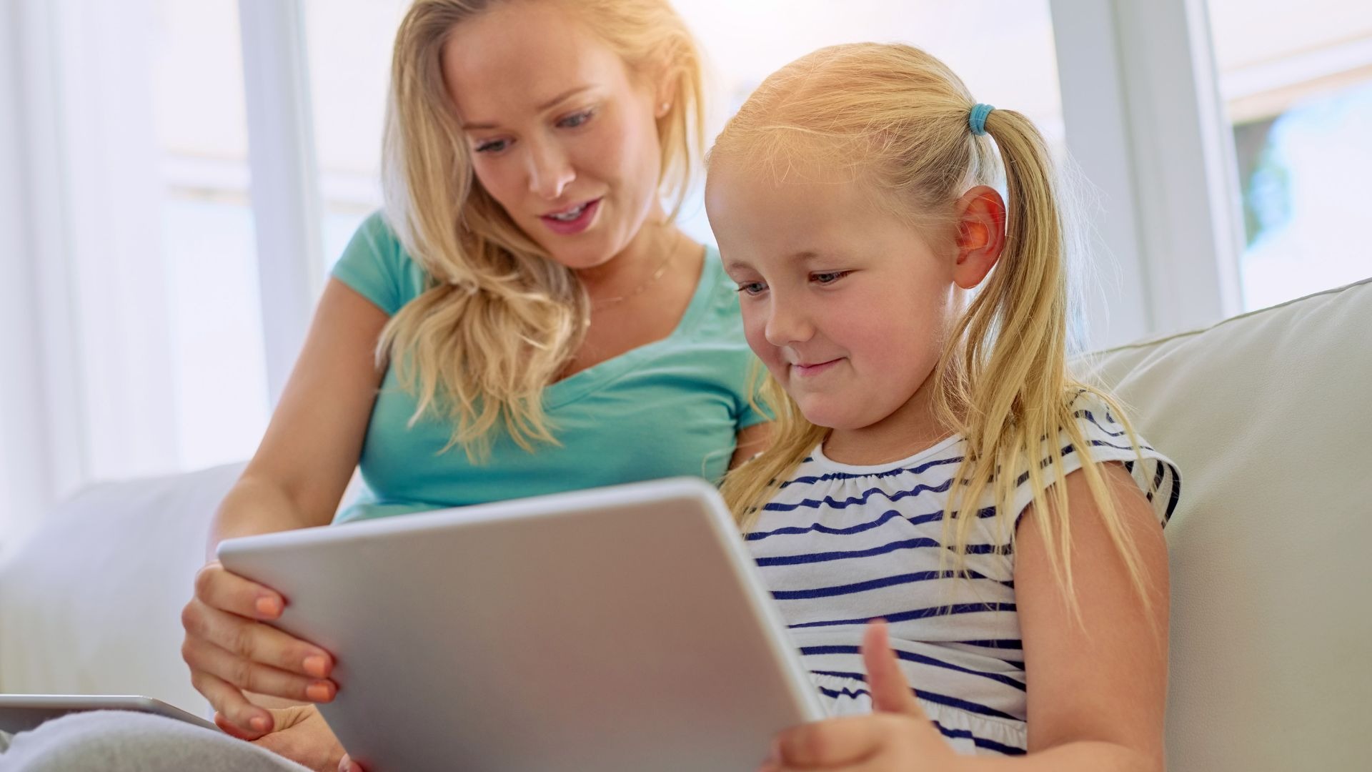 Mutter und kleines Kind sitzen zusammen auf dem Sofa und nutzen ein Tablet