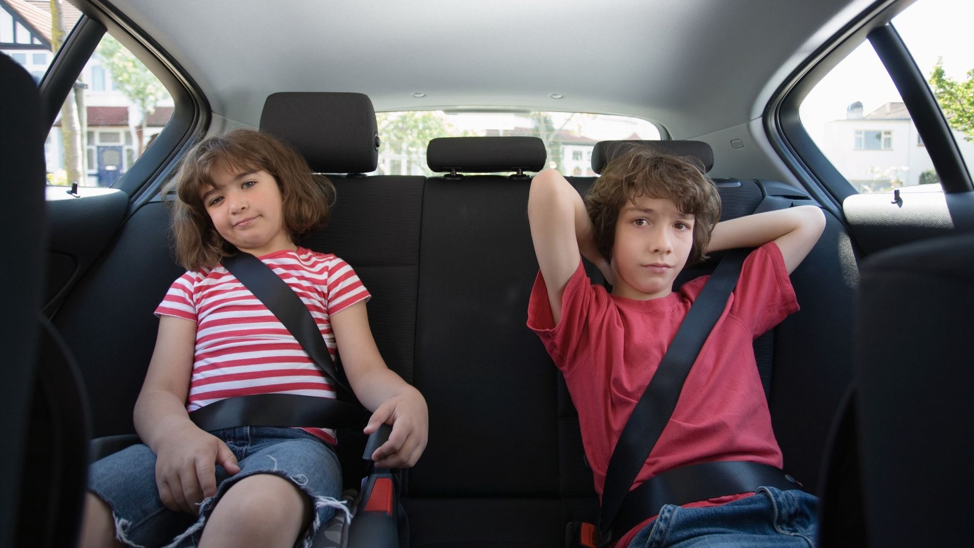 Ein Mädchen und ein Junge sitzen mit angelegten Sicherheitsgurten auf der Rückbank eines Autos