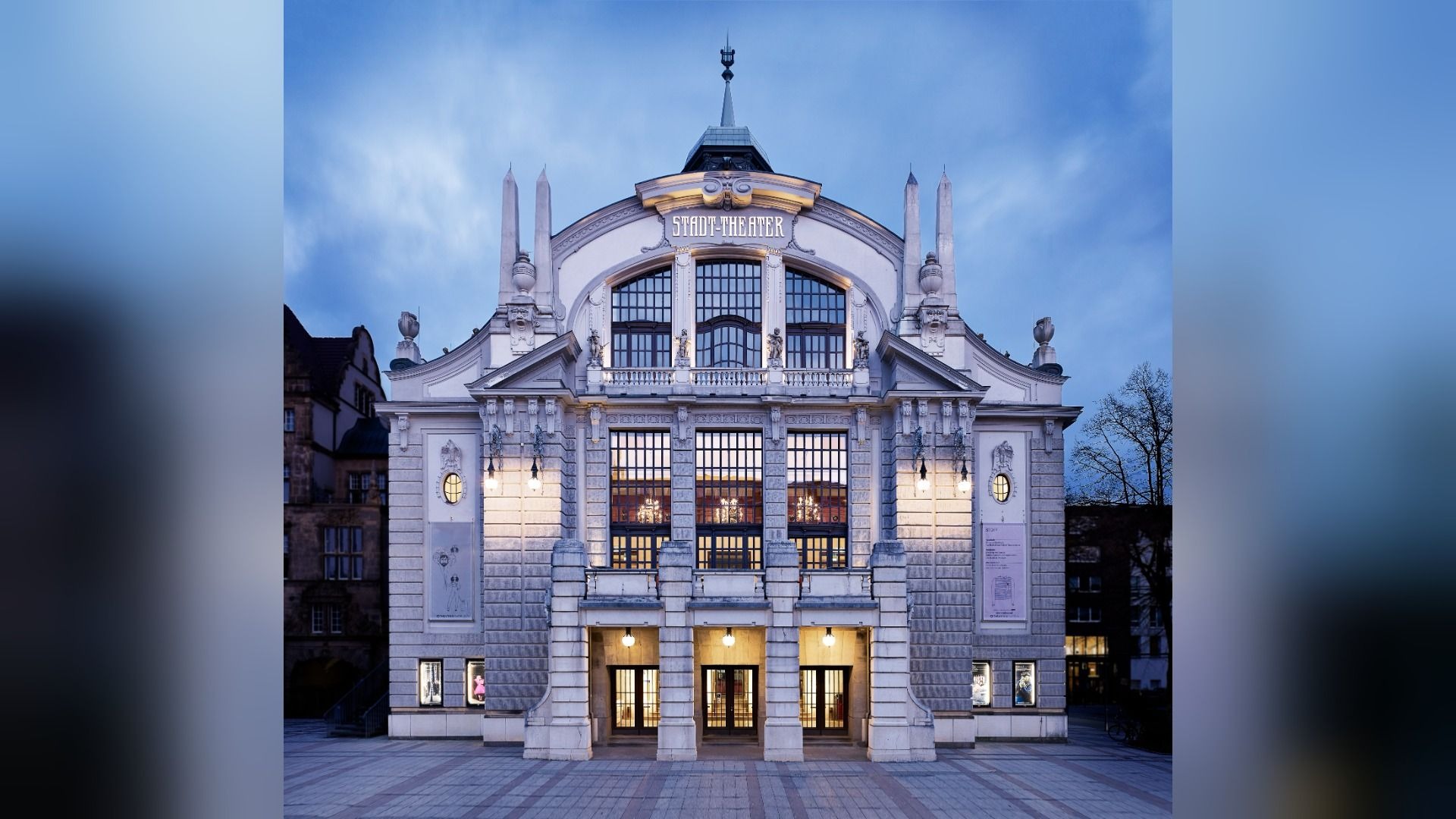 Prächtiges Gebäude des Stadt-Theaters bei Dämmerung, die Fenster und Eingänge sind hell beleuchtet
