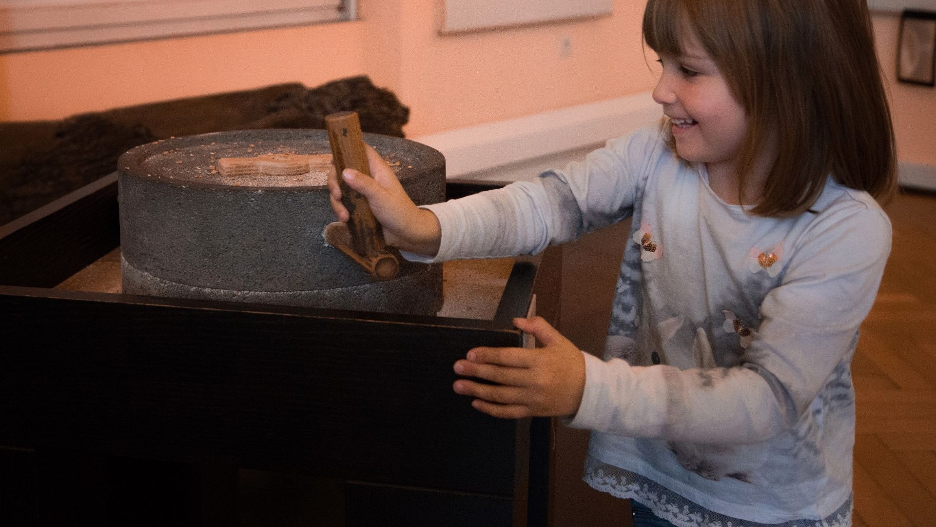Lachendes Kind bedient eine Handmühle aus Stein mit hellem Mahlgut