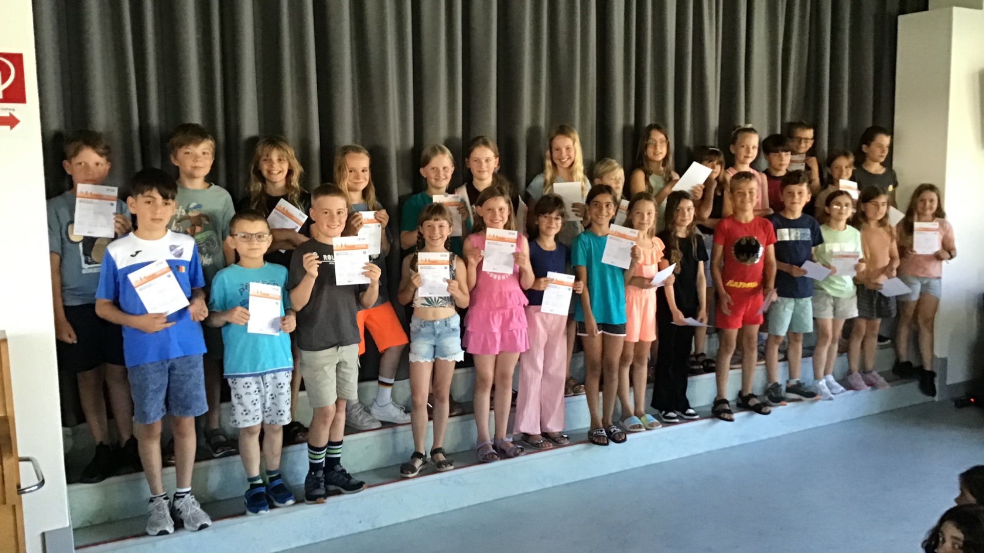 Eine Gruppe lächelnder Grundschulkinder der Grundschule Asemissen steht vor einem Vorhang und hält stolz ihre Urkunden