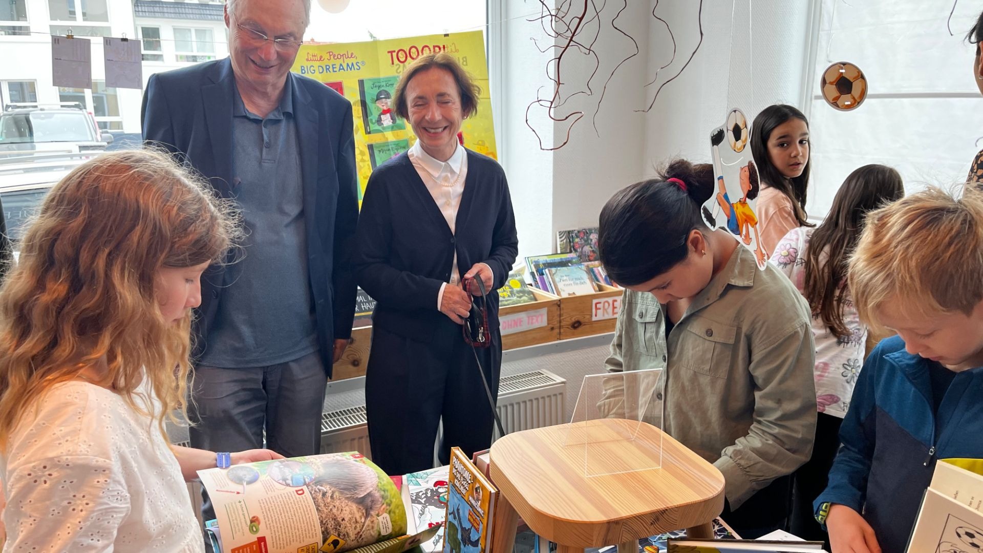 Mehrere Kinder der Grundschule Stieghorst wählen begeistert Bücher aus, während zwei Erwachsene lächeln