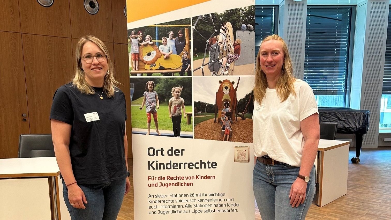 Zwei Frauen stehen lächelnd neben einem Banner mit der Aufschrift „Ort der Kinderrechte“ und Logos vom Kreis Lippe