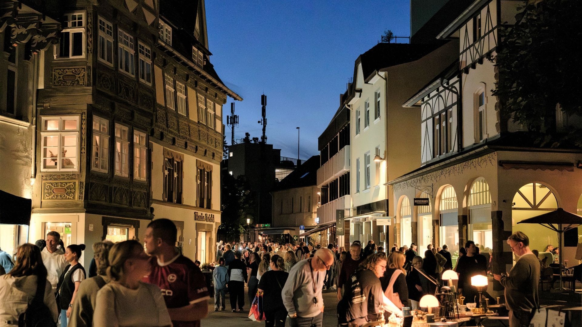 Eine Menschenmenge bummelt abends über einen beleuchteten Abendmarkt zwischen Fachwerkhäusern und Geschäften