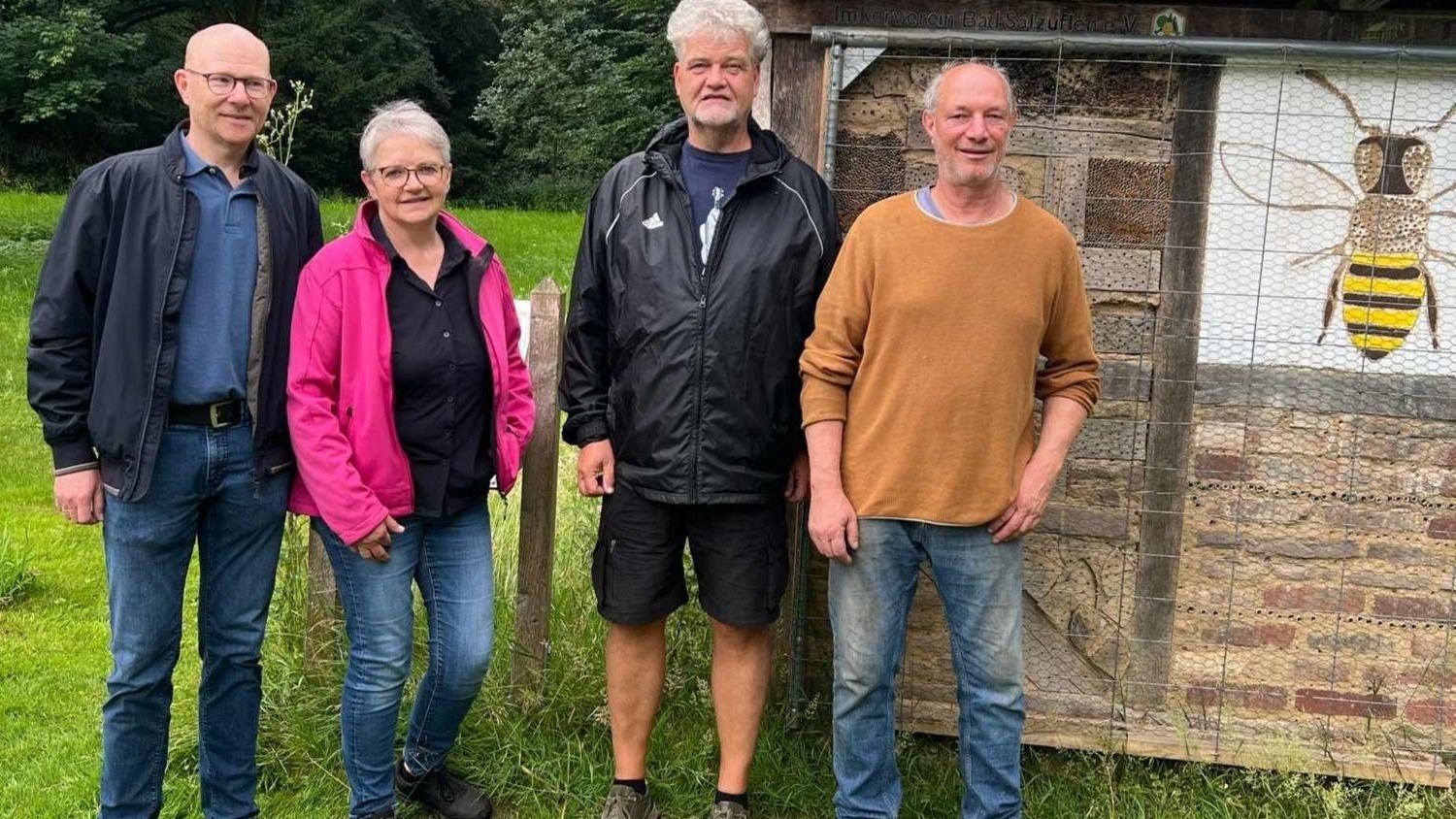 Vier Personen vor einer Insektennisthilfe mit Bienenmotiv in einem Landschaftsgarten