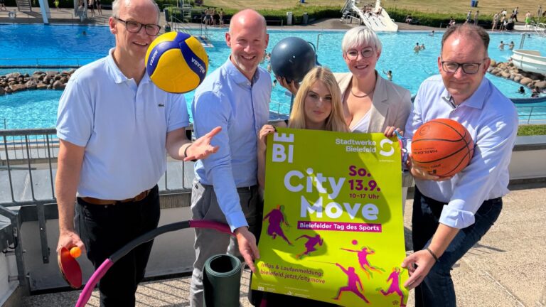 Fünf Personen halten ein grünes Plakat für den "City Move Bielefeld" und Sportgeräte an einem Schwimmbad
