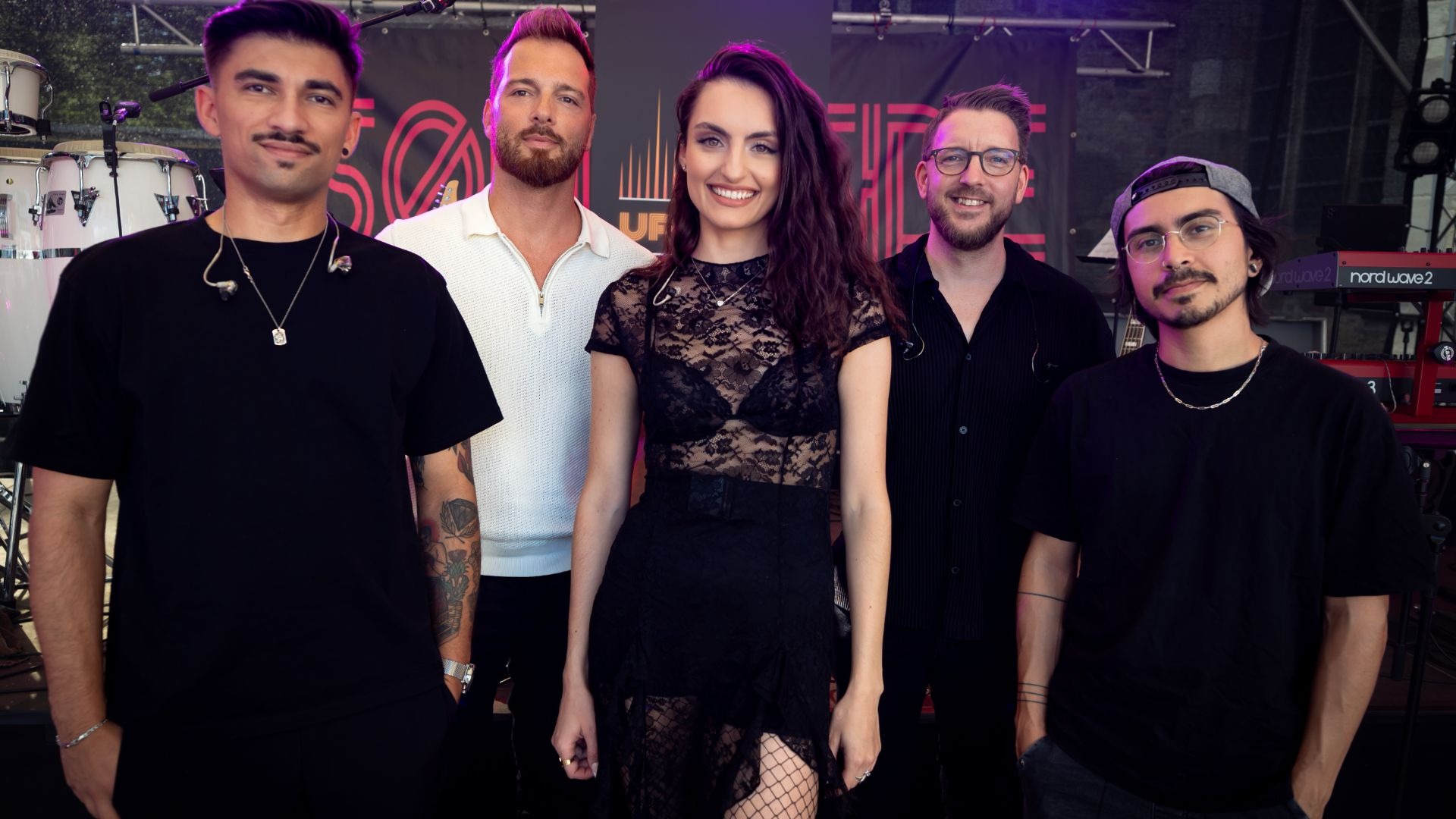 Eine Frau und vier Männer der Band UpTones lächeln auf einer Bühne mit Instrumenten