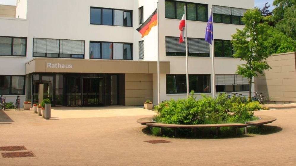 Weißes Rathausgebäude mit "Rathaus"-Schriftzug, deutschen, polnischen und EU-Flaggen, davor ein Platz mit Bänken und