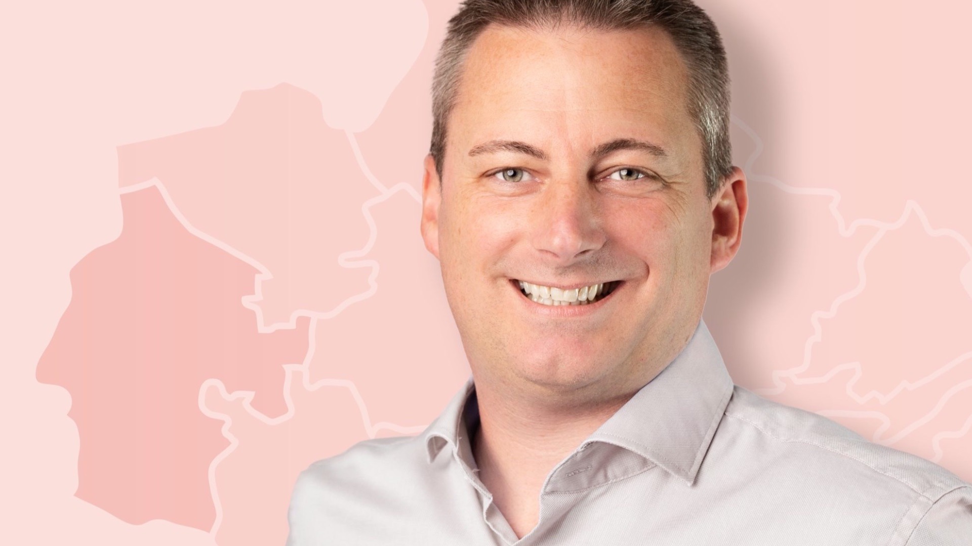 Nicolai Trettin lächelt in die Kamera, im hellen Hemd vor einem rosa Hintergrund mit Landkartenumrissen