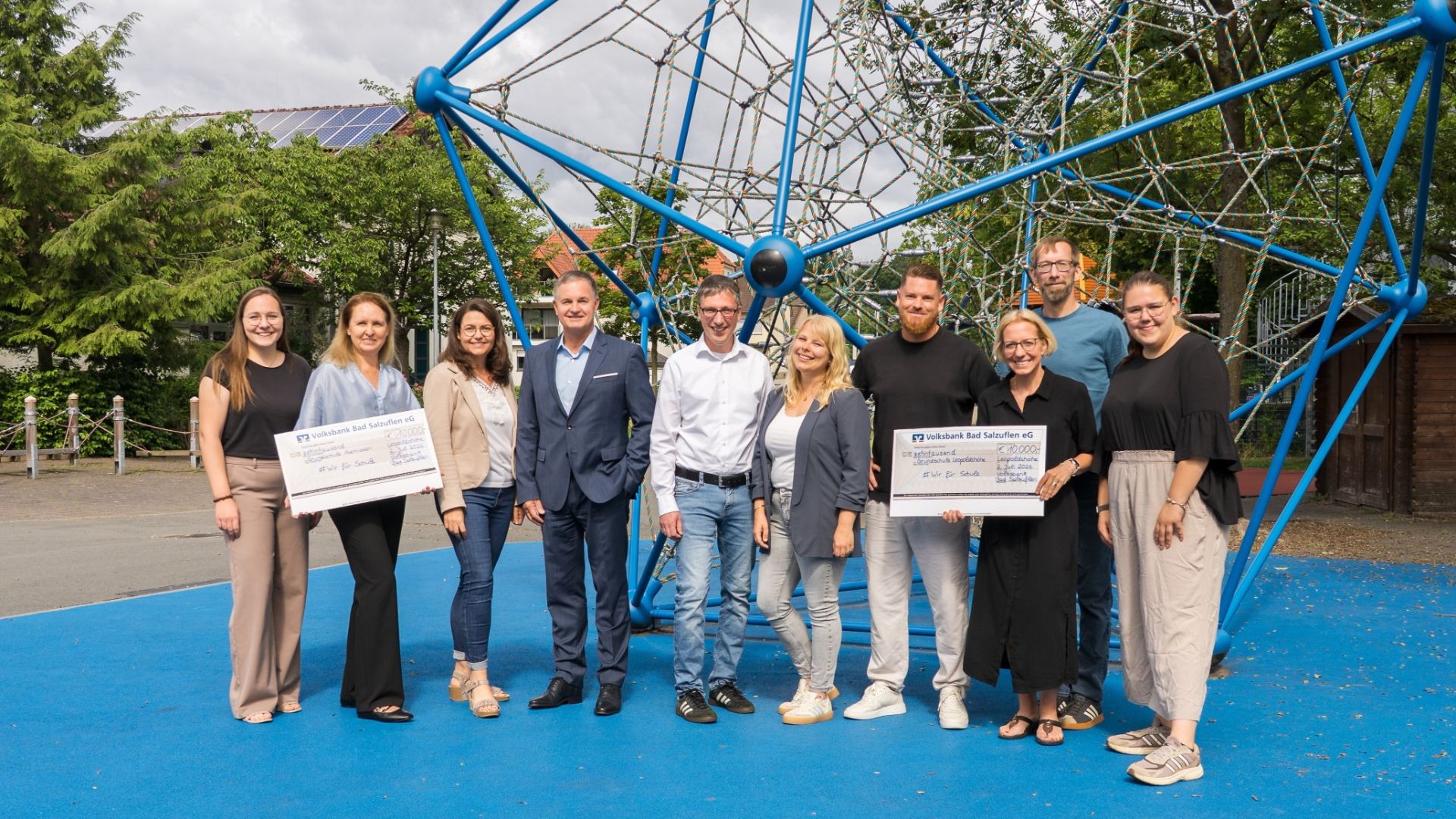 Zehn Personen halten zwei 10.000 Euro-Schecks der Volksbank Bad Salzuflen eG für Schulen vor einem blauen Kletternetz