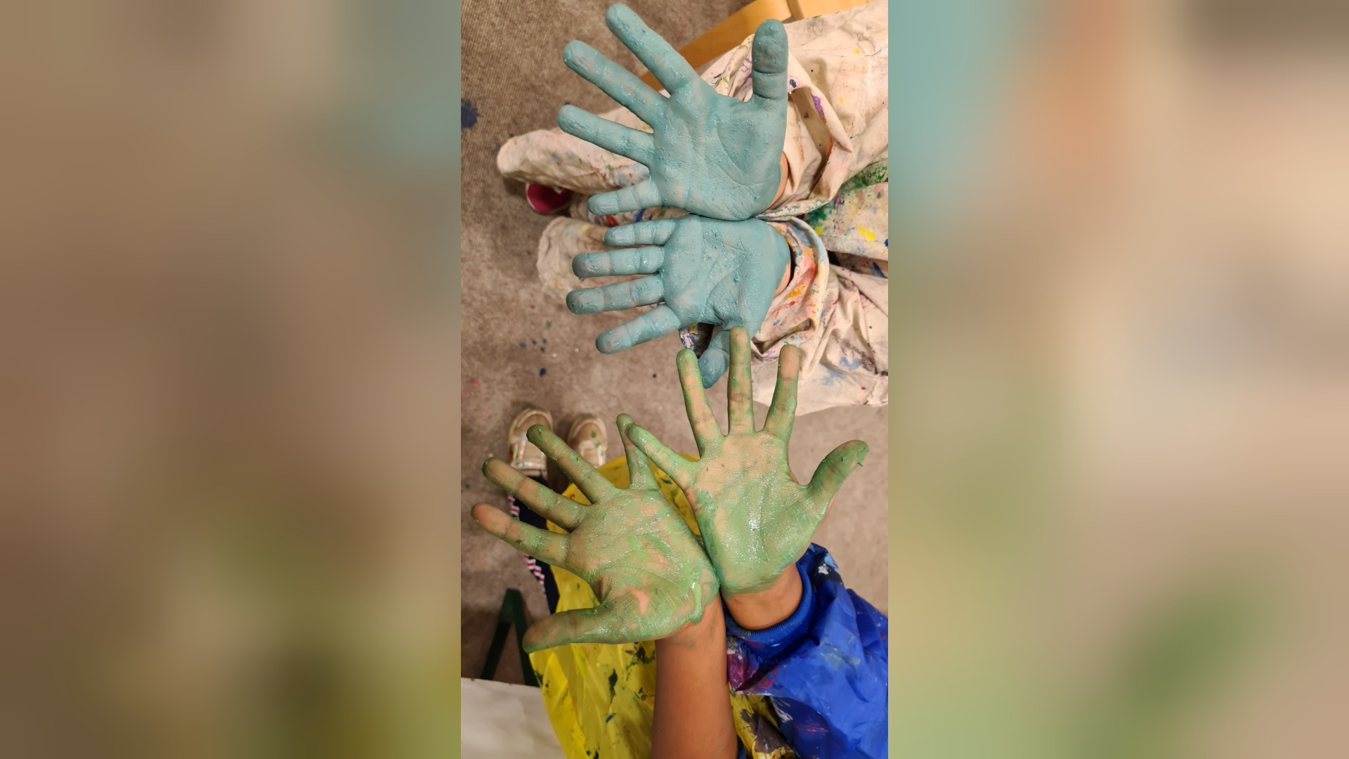 Vier bemalte Hände, zwei blau und zwei grün, von Kindern in farbigen Malkitteln