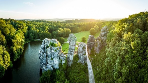 Die Externsteine, markante Felsformationen, umgeben von einem See und dichtem Wald im goldenen Abendlicht