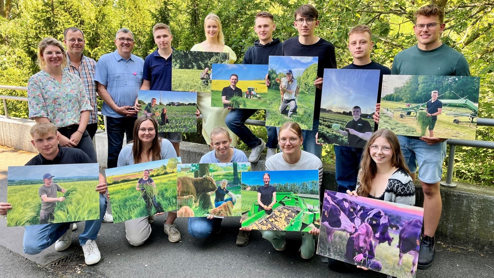 Fünfzehn Personen, viele junge Landwirte, halten draußen vor grünen Bäumen Plakate mit Landwirtschaftsmotiven