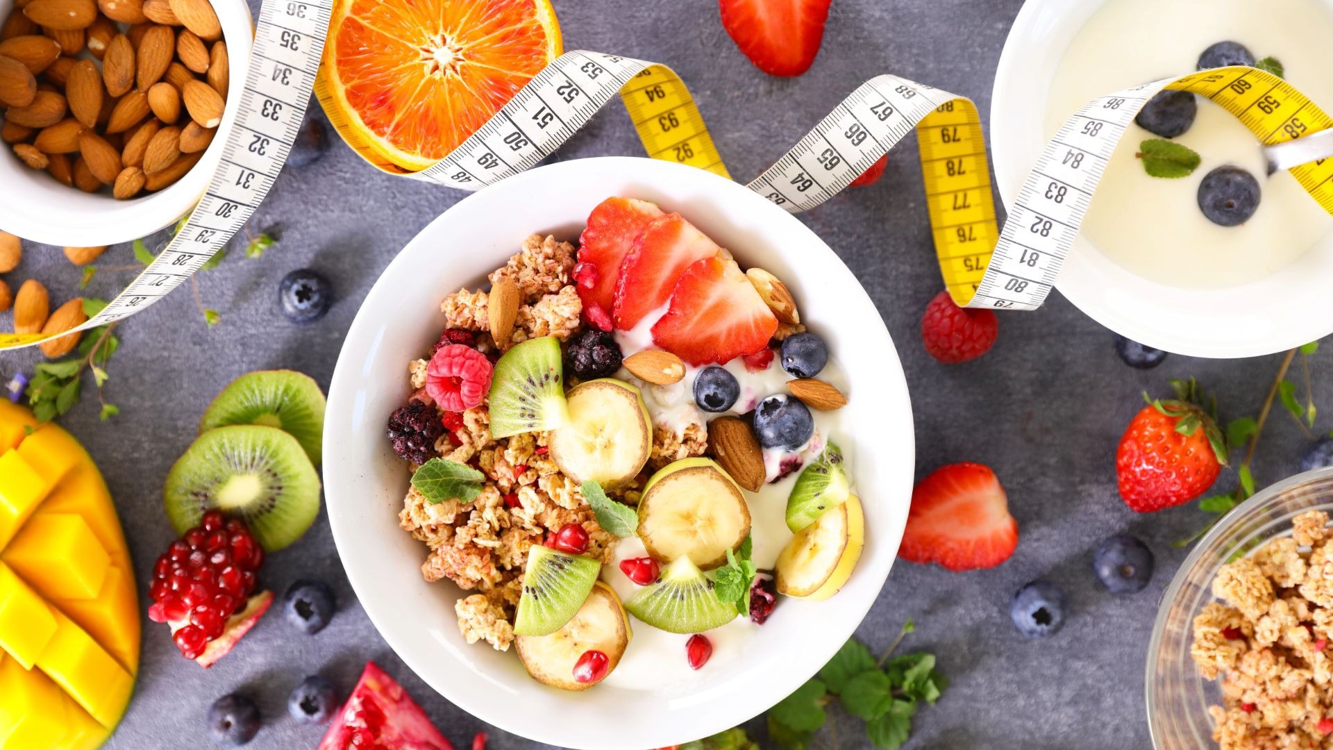 Müslischale mit frischen Früchten, Joghurt und Nüssen umgeben von einem Maßband und weiteren gesunden Zutaten