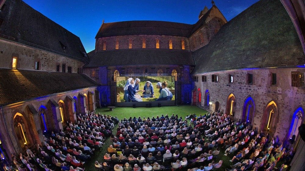 Zahlreiche Zuschauer sehen Open-Air-Kino im erleuchteten Kreuzgarten des Klosters Alpirsbach bei Nacht