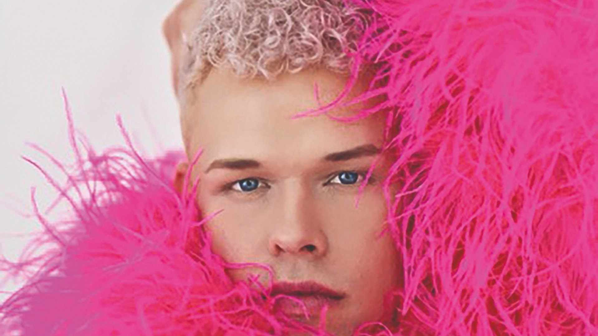 Tobias Born mit hellblauen Augen und kurzen, blonden Locken, umrahmt von leuchtend pinken Federn