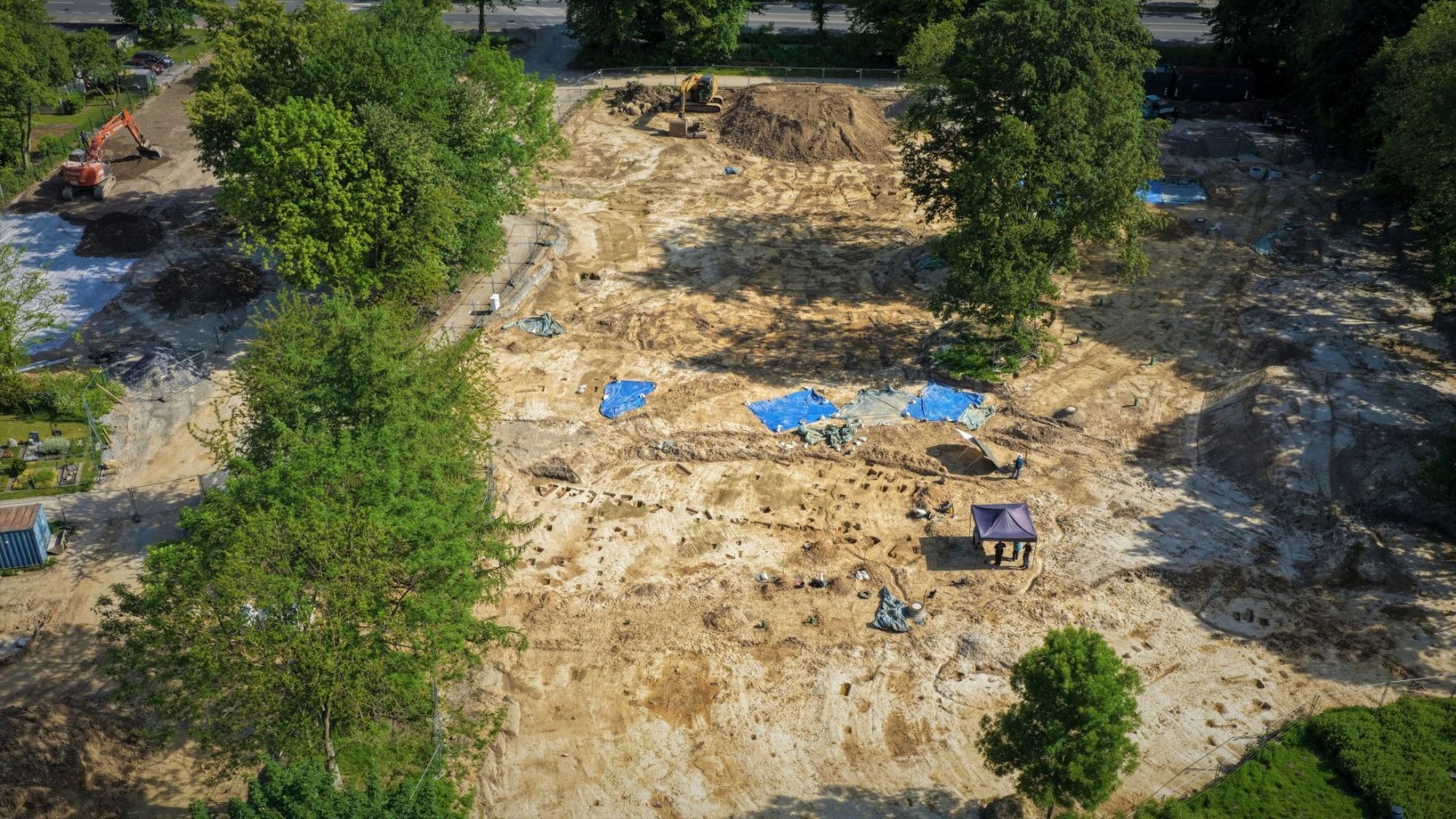Luftaufnahme einer großen archäologischen Ausgrabungsstätte mit Baggern, Zelten und freigelegten Strukturen im Boden