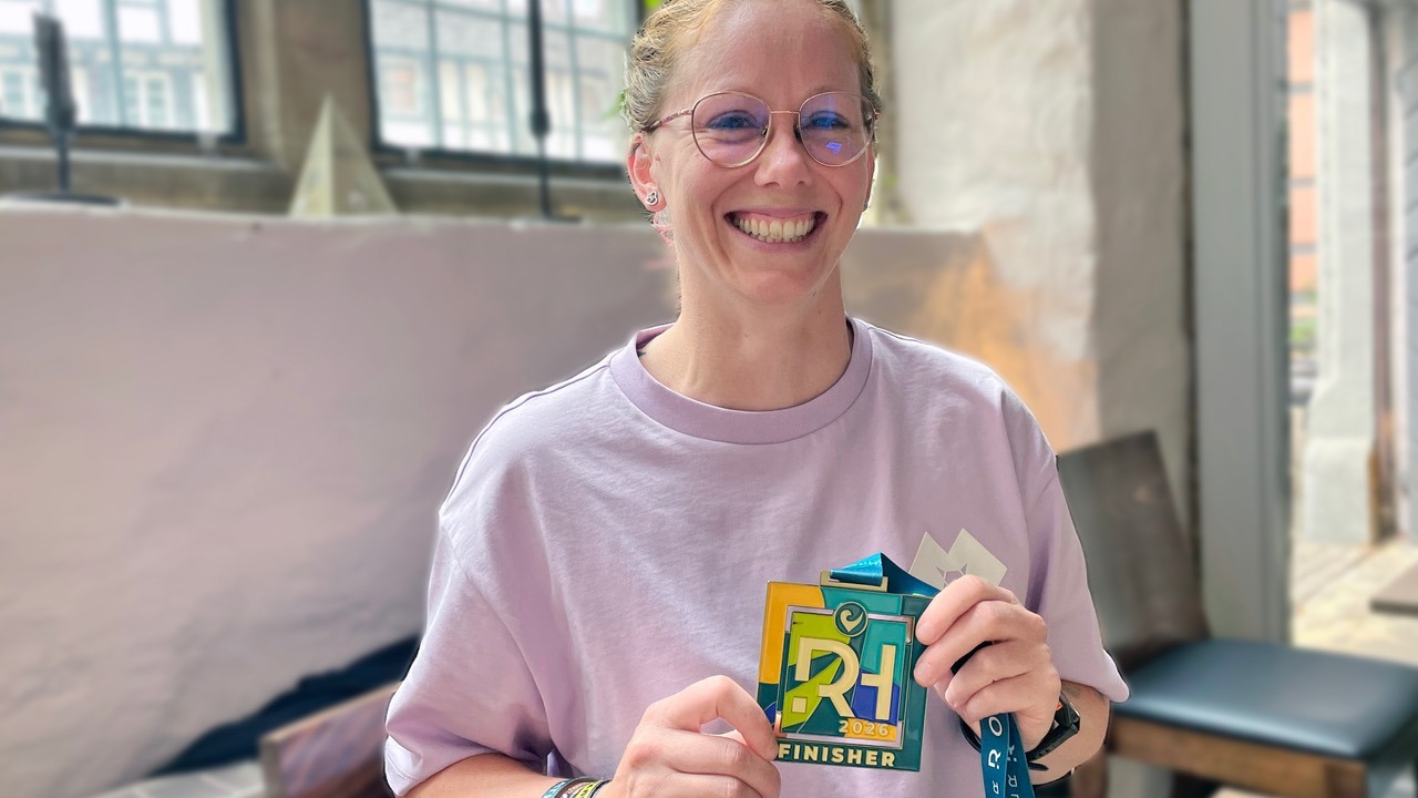 Lächelnde Frau mit Brille hält eine bunte Triathlon-Finisher-Medaille der DATEV Challenge Roth 2022