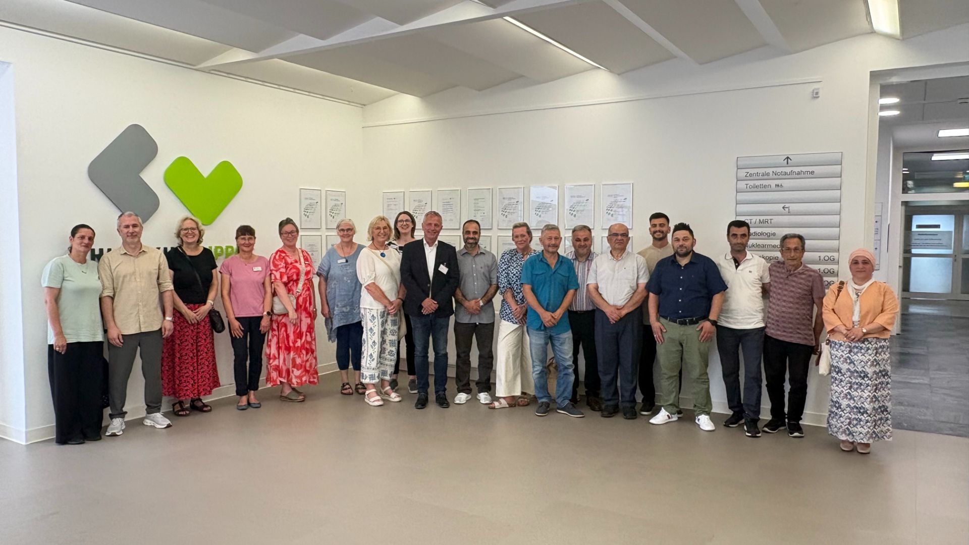 Gruppe von Männern und Frauen im Flur des Klinikums Lippe vor Wand mit Logo und Notaufnahme-Schildern