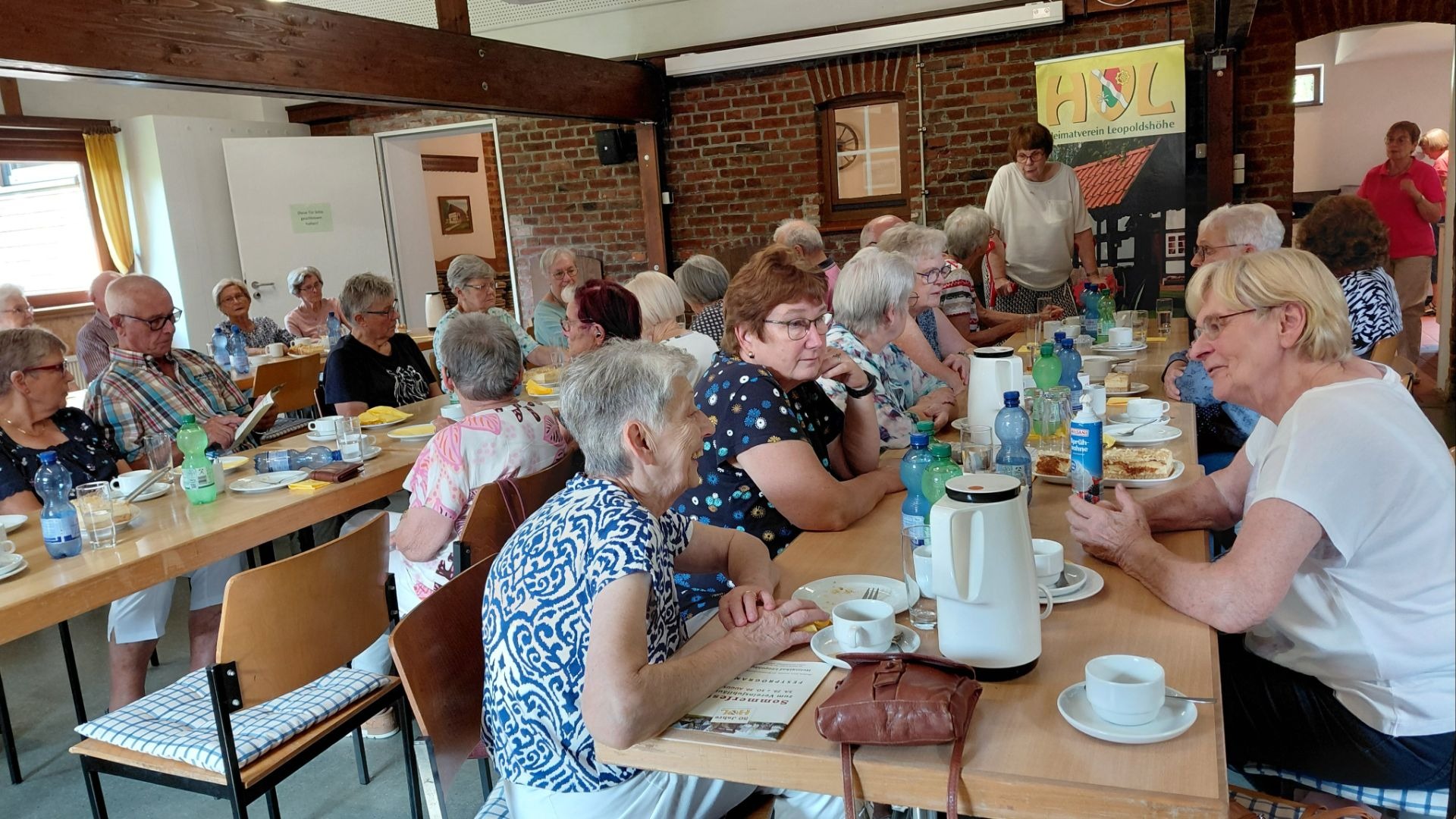 Senioren sitzen im Raum des Heimatvereins Leopoldshöhe an Tischen bei Kaffee und Kuchen zusammen und unterhalten sich