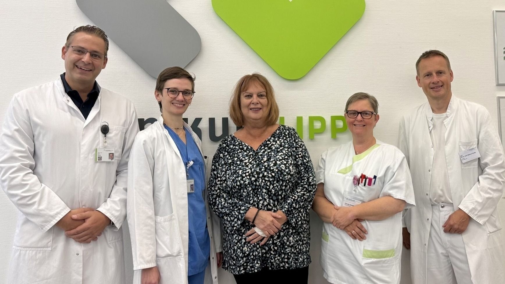 Fünf lächelnde Personen, davon drei Ärzte in weißen Kitteln und zwei Frauen, vor der Wand des Klinikum Lippe