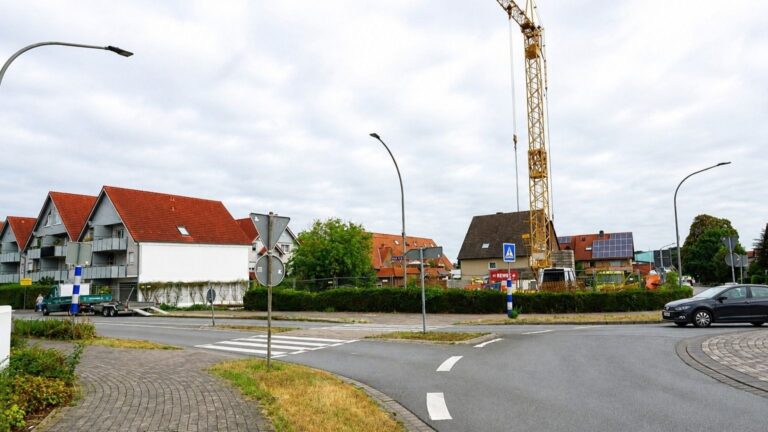 Straßenkreuzung mit modernen Wohngebäuden, einem Baugelände mit Kran, älteren Häusern und einem fahrenden Auto