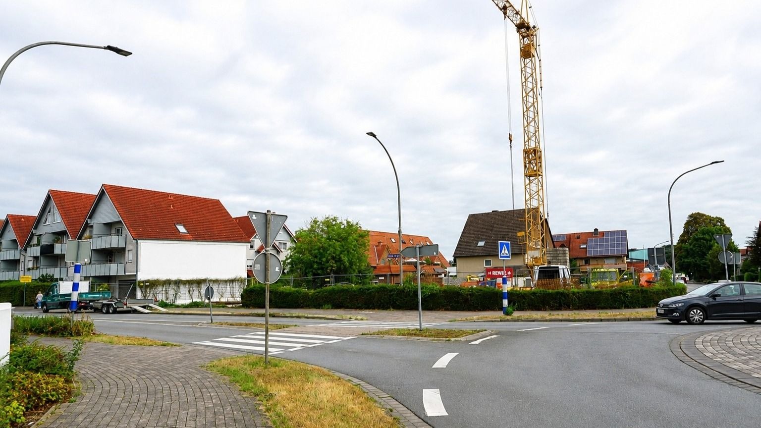 Straßenkreuzung mit modernen Wohngebäuden, einem Baugelände mit Kran, älteren Häusern und einem fahrenden Auto