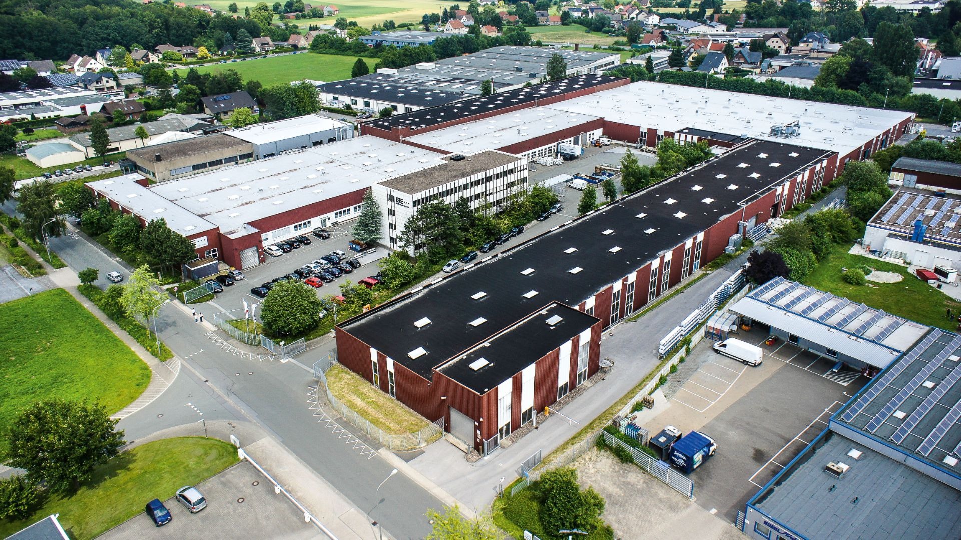 Luftaufnahme des BE Bauelemente Fabrikgeländes in Greste mit vielen Gebäuden, Parkplätzen und grünen Flächen