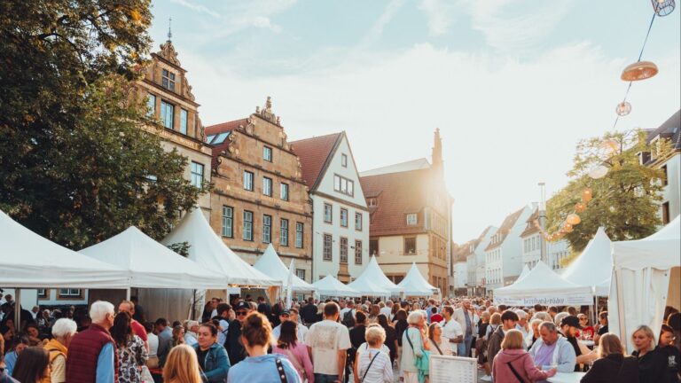 Viele Menschen schlendern zwischen weißen Verkaufsständen auf einem belebten Weinmarkt in einer Altstadt bei