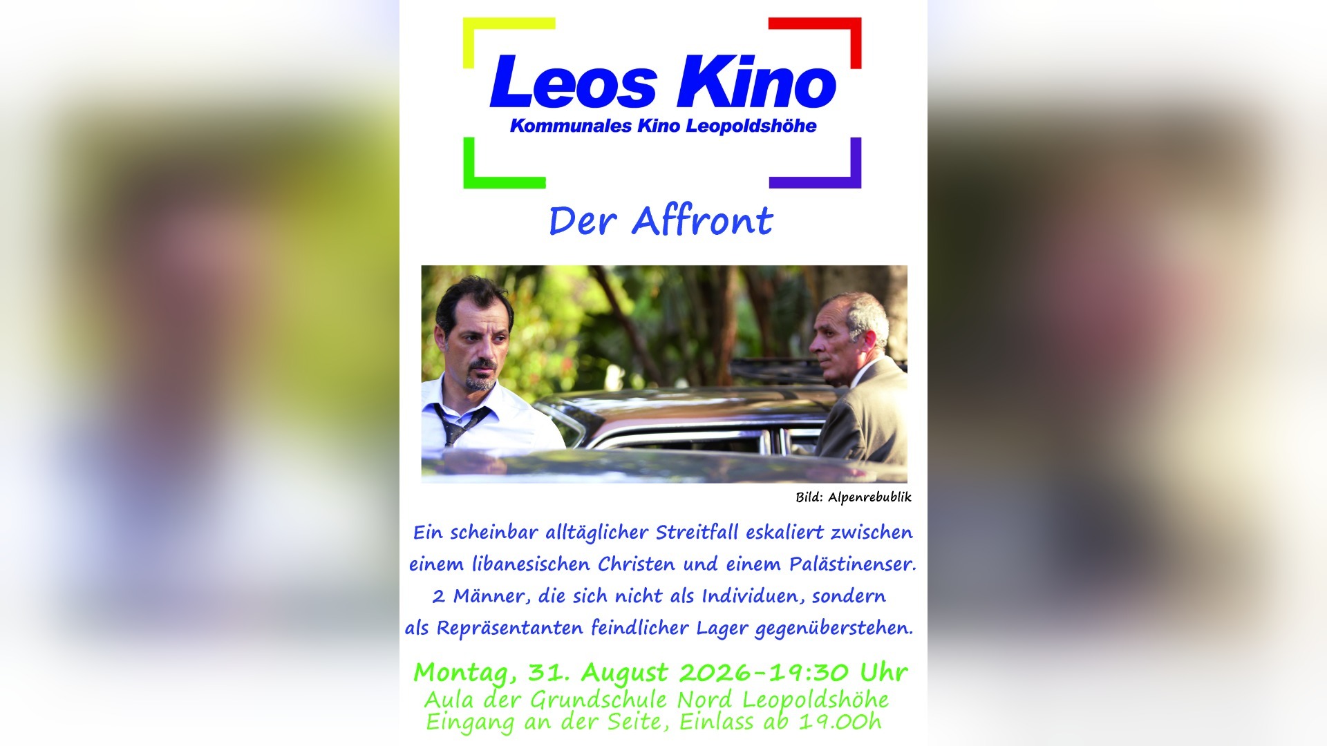 Zwei Männer mit ernsten Gesichtern stehen sich im Freien gegenüber, zwischen ihnen ist ein Auto erkennbar
