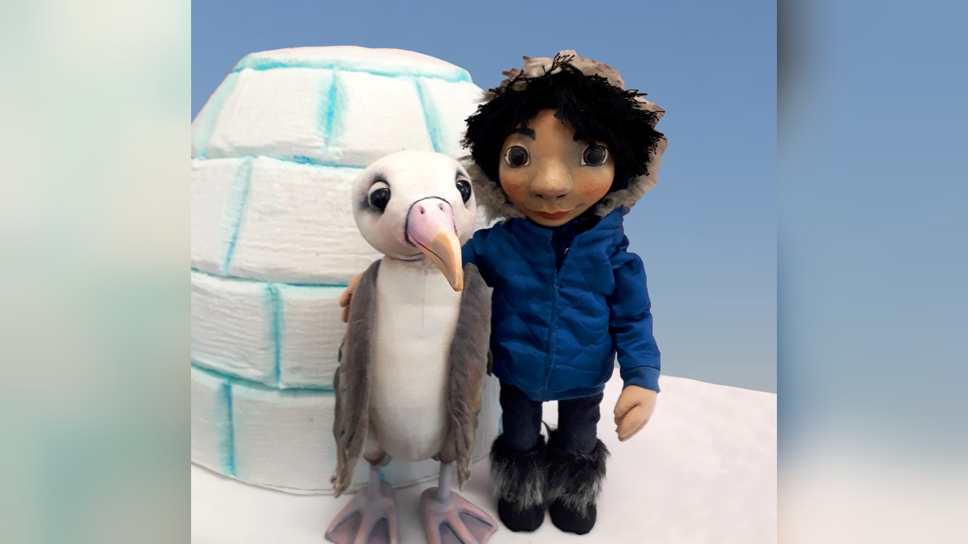 Albatros Albi und eine menschliche Figur in blauer Winterkleidung umarmen sich vor einem Iglu auf Schnee