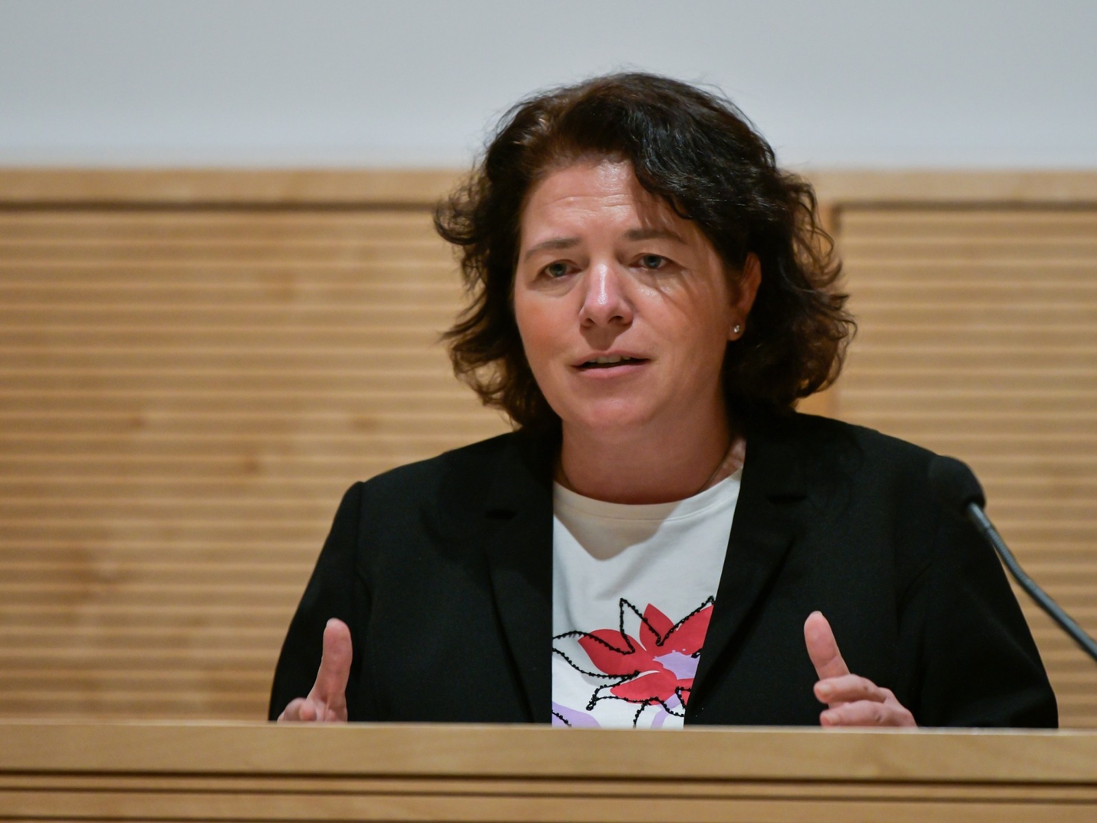 Kerstin Vieregge spricht an einem Pult vor einer Holzwand und gestikuliert mit den Händen