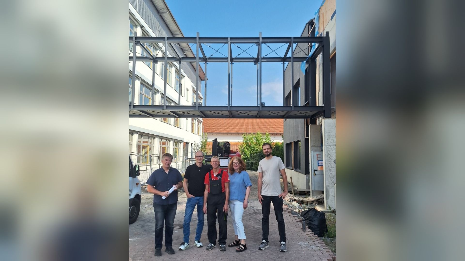 Fünf Personen stehen unter der neuen Stahl-Verbindungsbrücke zwischen zwei Gebäuden der Grundschule Helpup