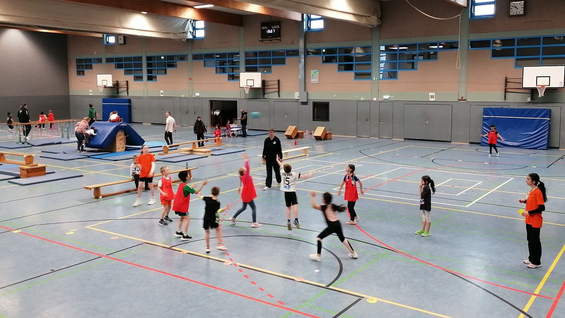 Kinder und Erwachsene beim Handballtraining und Turnen an verschiedenen Geräten in einer Sporthalle