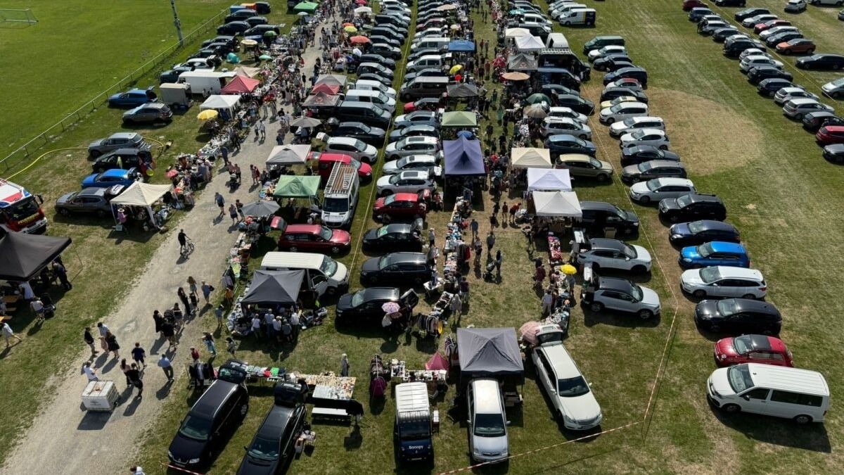 Flohmarkt auf einem Rasenplatz mit parkenden Autos, Verkaufsständen und vielen Besuchern