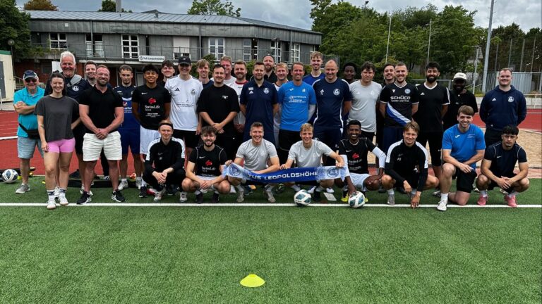 Große Gruppe von Personen posiert auf einem Kunstrasen-Sportplatz, einige halten ein blaues Banner "FÜR LEOPOLDSHÖHE