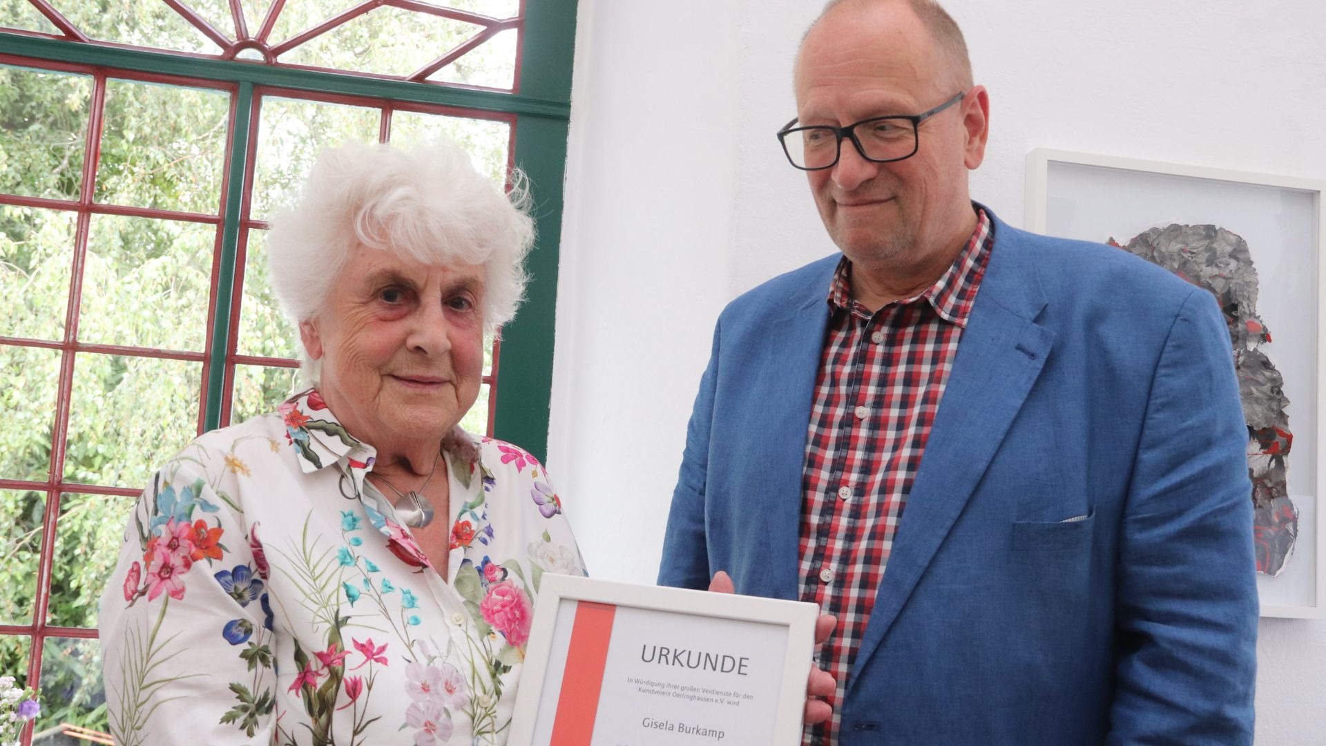 Mann mit Brille überreicht Gisela Burkamp eine gerahmte Urkunde des Kunstvereins Oerlinghausen
